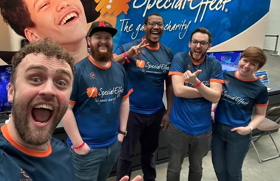 Selfie of five smiling people in SpecialEffect shirts standing in front of an expo stand