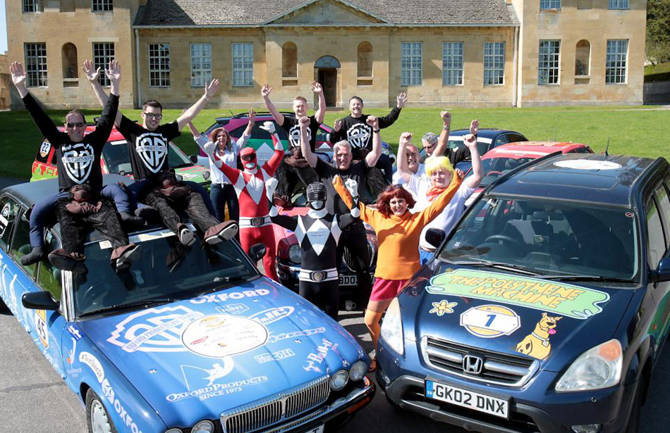 Group of people, some in costume, waving from behind two decorated cars