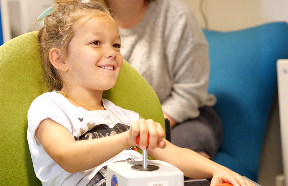 Smilinmg young girl using an adapted joystick and button switch to play a video game