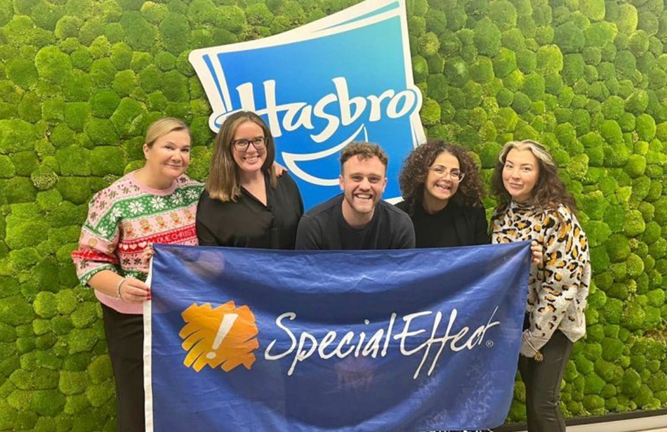 group of five smiling people holding a SpecialEffect flag